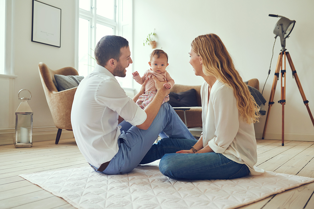 Proud mother and father smiling at their newborn baby daughter, sitting on the floor at home