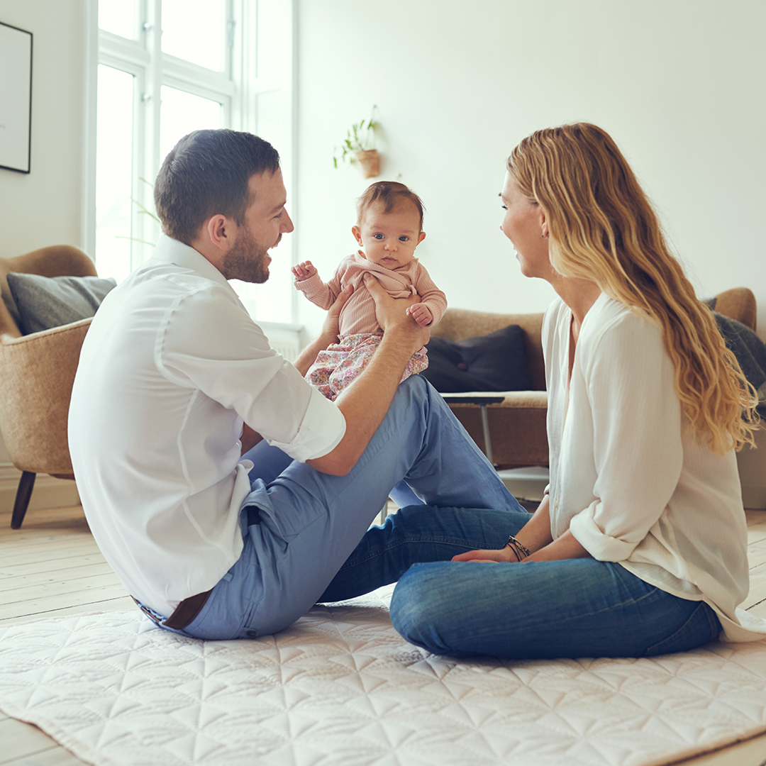 Proud mother and father smiling at their newborn baby daughter, sitting on the floor at home