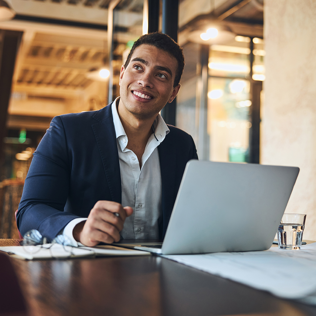 Joyous young draftsman daydreaming in the workplace Portrait of a handsome smiling dreamy male engineer sitting at the laptop in the office