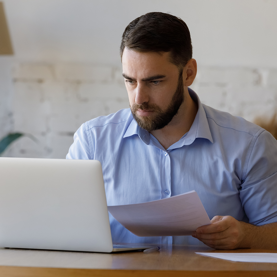 Focused millennial business man checking paper reports. Entrepreneur reviewing financial document at laptop. Homeowners paying rent bills, invoice, reading mortgage, loan, credit notice from bank,